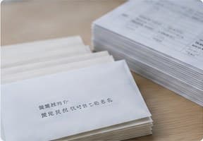 机に積まれた白い封筒の束と宛名リスト